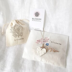 May include: A small, cream-colored drawstring bag and a white paper package with the word "blossom" printed on them. The bag has a floral design and the word "blossom" printed on it. The package is decorated with dried flowers and a ceramic heart.