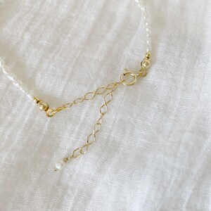 May include: A delicate pearl necklace with a gold chain extender. The necklace is made of small, white pearls and has a simple, elegant design.