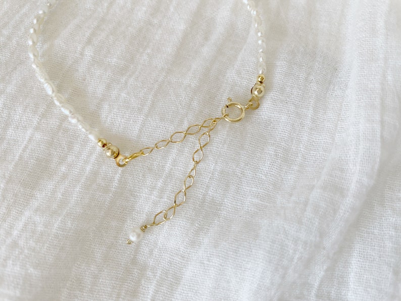 May include: A delicate pearl necklace with a gold chain extender. The necklace is made of small, white pearls and has a simple, elegant design.