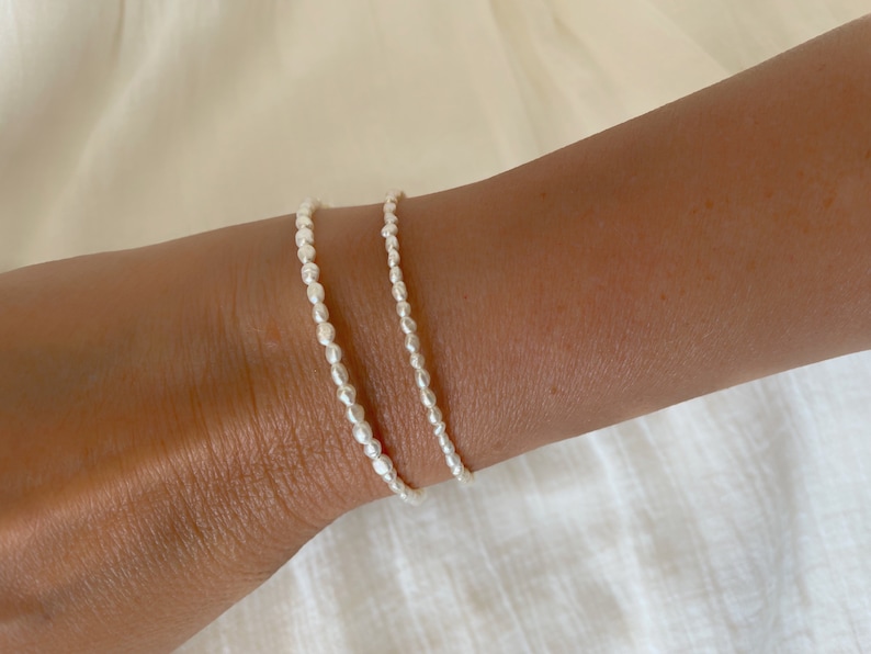 May include: Two delicate pearl bracelets on a wrist. The bracelets are made of small, white pearls strung together on a silver chain.