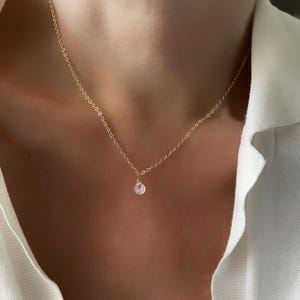 Puede incluir: Un delicado collar de cadena de oro con un pequeño colgante de piedra preciosa iridiscente.