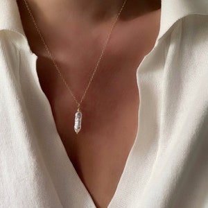 May include: A delicate gold chain necklace with a single, large, irregular pearl pendant.