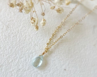 Puede incluir: Un delicado collar de cadena dorada con un colgante de piedra preciosa azul claro en forma de lágrima.