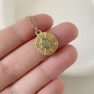 May include: Gold necklace with a round pendant featuring a green gemstone surrounded by a textured design.
