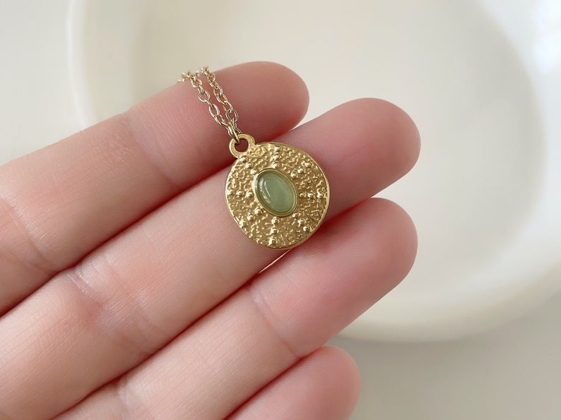 May include: Gold necklace with a round pendant featuring a green gemstone surrounded by a textured design.