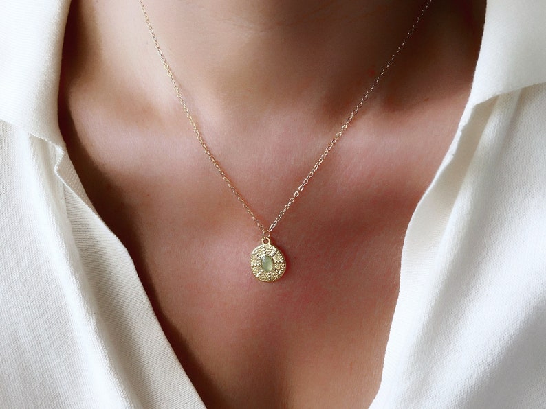 A gold chain necklace with a round pendant featuring a green stone surrounded by a textured design.