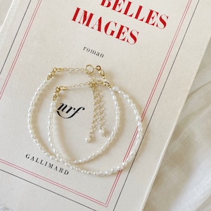 May include: Two delicate pearl bracelets with gold clasps, layered on a white book with the text "BELLES IMAGES roman GALLIMARD" printed on the cover.