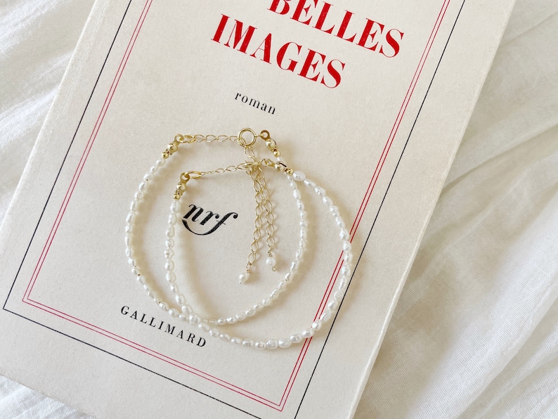May include: Two delicate pearl bracelets with gold clasps, layered on a white book with the text "BELLES IMAGES roman GALLIMARD" printed on the cover.