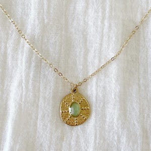 A gold chain necklace with a round pendant featuring a green stone surrounded by a detailed design.
