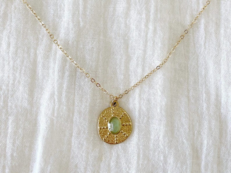A gold chain necklace with a round pendant featuring a green stone surrounded by a detailed design.
