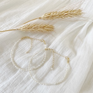 May include: Two delicate pearl necklaces with gold chain accents, displayed on a white fabric background.