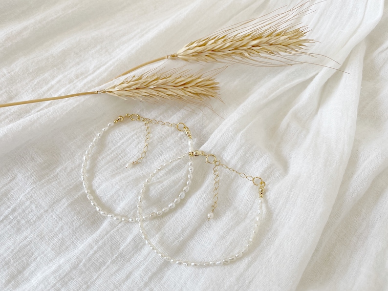 May include: Two delicate pearl necklaces with gold chain accents, displayed on a white fabric background.