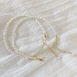 May include: Two delicate pearl necklaces with a gold chain connector. The necklaces are layered and feature small, white pearls.