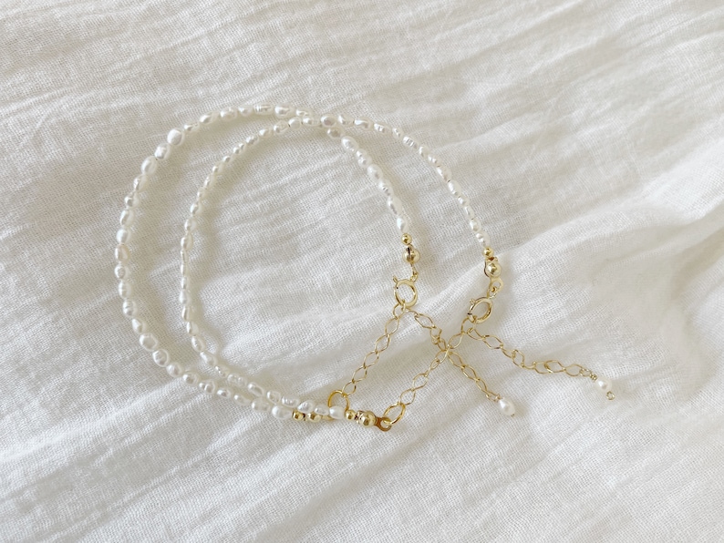 May include: Two delicate pearl necklaces with a gold chain connector. The necklaces are layered and feature small, white pearls.