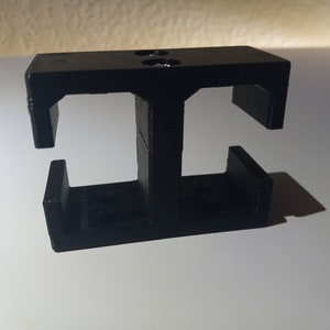 May include: Black plastic 3D printed object with two open slots. The object has a rectangular base and two vertical supports.