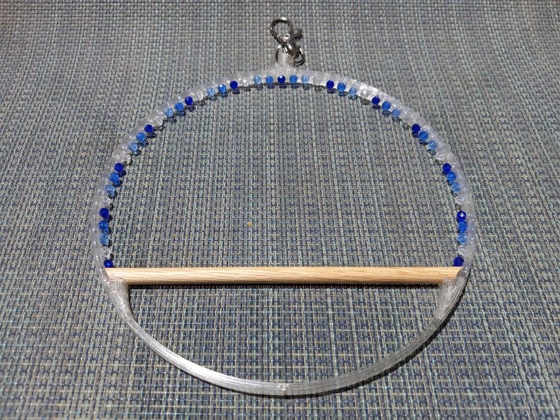 May include: Clear acrylic bird perch with a wooden dowel and a ring for hanging. The perch is decorated with blue and clear beads. A metal clasp is attached to the top for easy hanging. This bird perch is a decorative and functional accessory for pet birds.