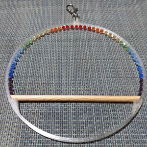 May include: Clear acrylic bird perch with a rainbow of colorful beads. The perch has a wooden dowel for the bird to sit on and a metal clip for hanging. A decorative and functional bird accessory.