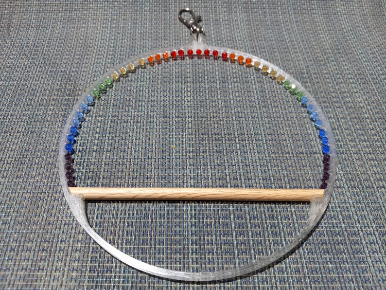 May include: Clear acrylic bird perch with a rainbow of colorful beads. The perch has a wooden dowel for the bird to sit on and a metal clip for hanging. A decorative and functional bird accessory.