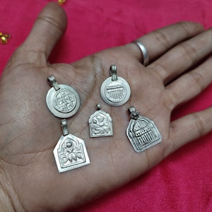 May include: Five silver pendants with intricate designs. The pendants are on a hand with a red background.
