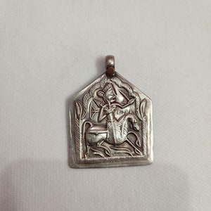 May include: Silver pendant with an intricate design of a figure riding a horse. The pendant is in the shape of a rectangle with rounded corners.
