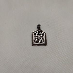 May include: A silver pendant with a rectangular shape and a design of two figures holding hands. The pendant has a loop at the top for attaching a chain.