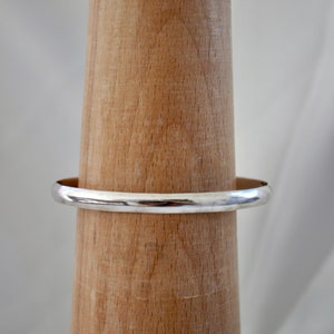 May include: A silver bangle bracelet on a wooden display stand.