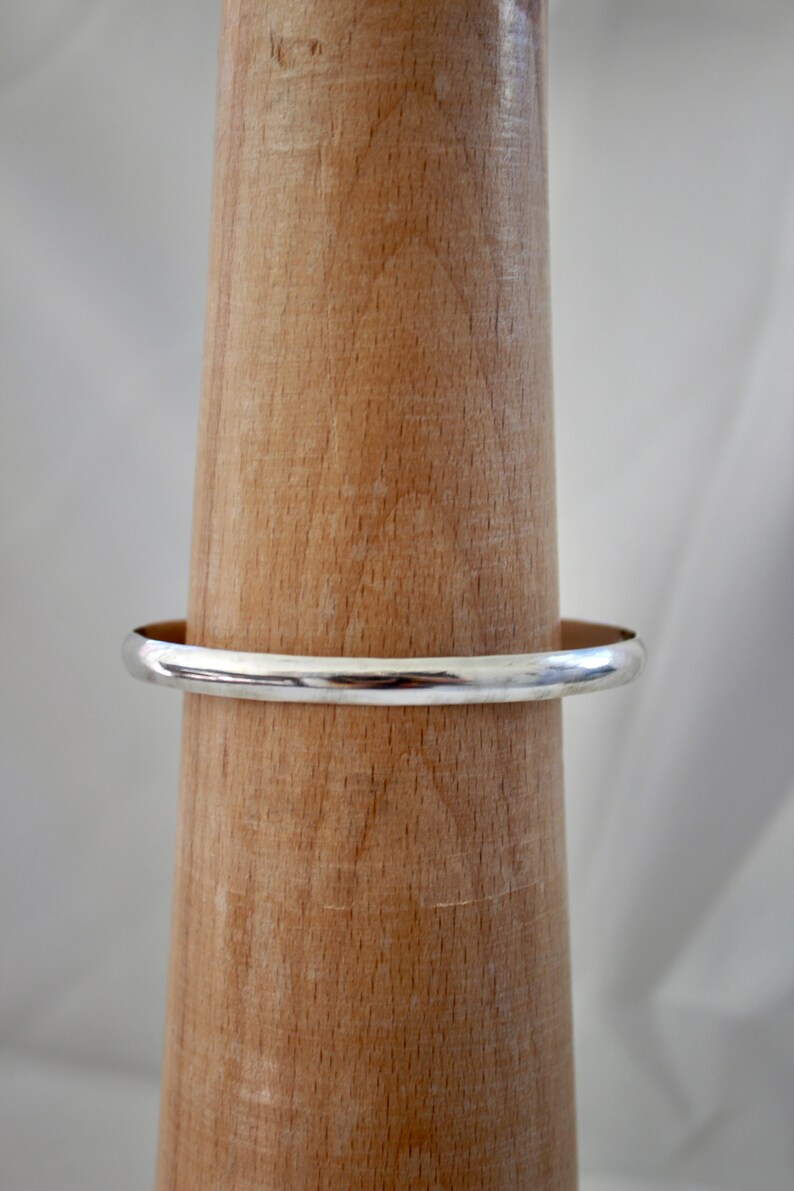 May include: A silver bangle bracelet on a wooden display stand.