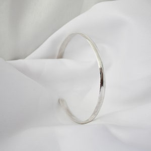 May include: A simple silver bangle bracelet with a smooth, polished finish.