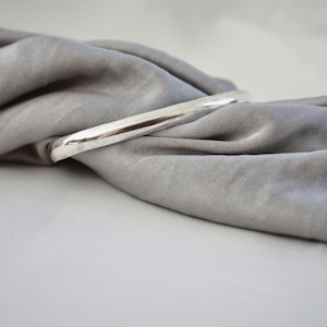 May include: A silver bangle bracelet on a grey fabric background.