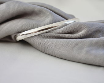 Puede incluir: Un brazalete de plata sobre un fondo de tela gris.