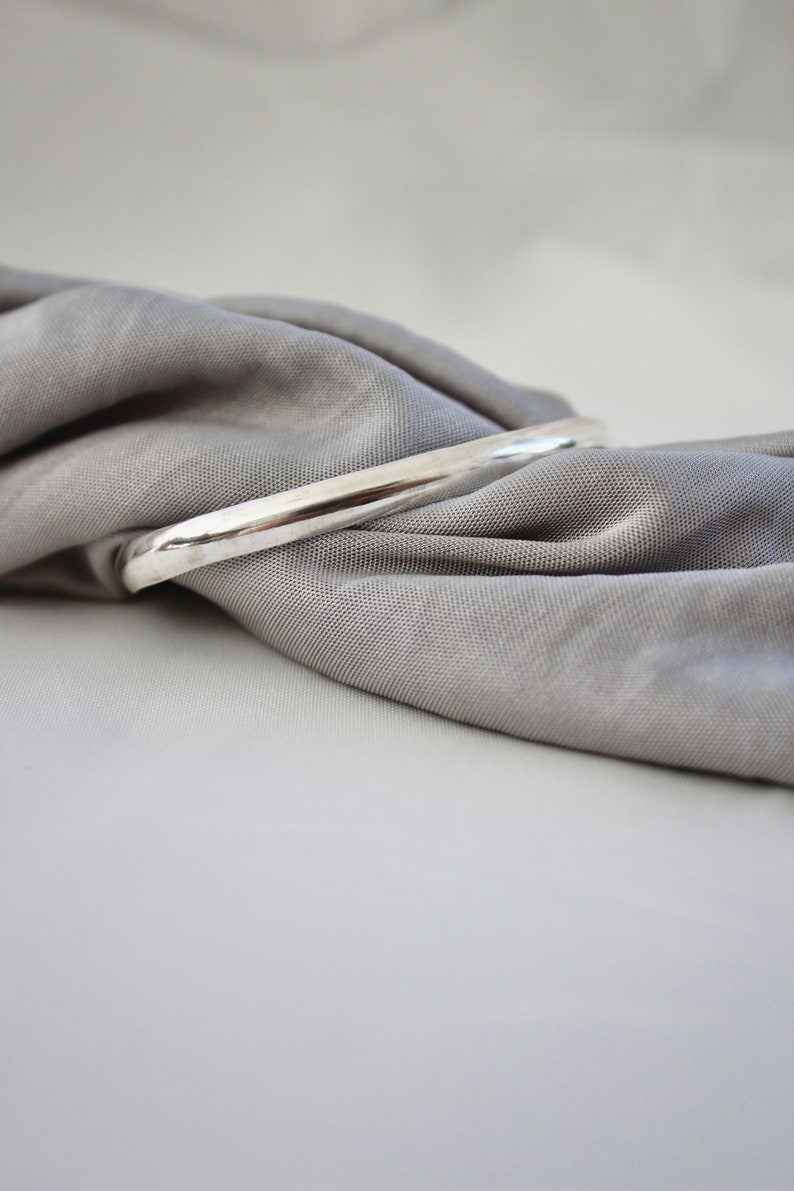 May include: A silver bangle bracelet on a gray fabric background.
