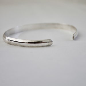 May include: A silver bangle bracelet with a smooth, rounded surface.