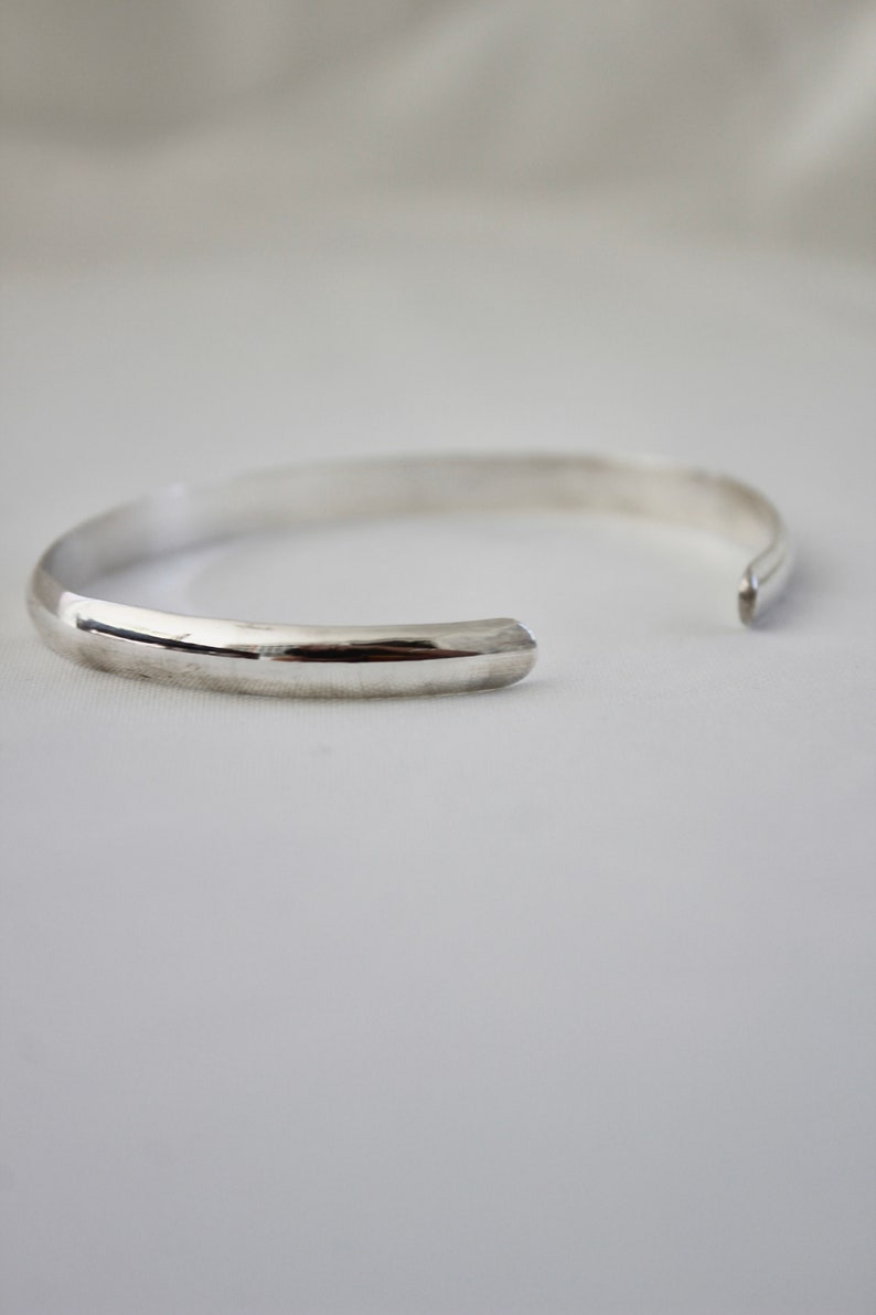 May include: A silver bangle bracelet with a smooth, rounded surface.