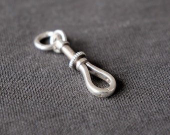 May include: A silver-colored clasp with a screw mechanism and a loop at each end. The clasp is designed with a textured screw and a smooth, curved hook. The background is a solid, dark gray.