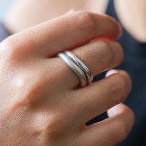 Può includere: Due anelli d'argento impilati su un dito. Gli anelli sono semplici e lisci, con una forma leggermente arrotondata.