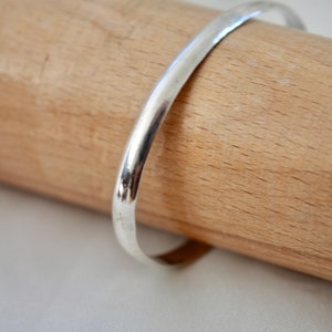 May include: A simple silver bangle bracelet, shown on a wooden surface.