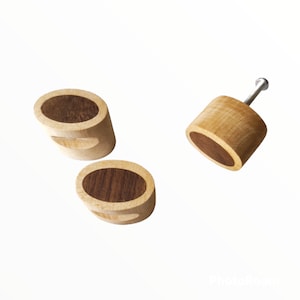 Könnte beinhalten: Drei Holzknaufknöpfe mit dunkler Holzeinlage. Die Knöpfe sind oval geformt und haben ein einzelnes Schraubenloch oben.