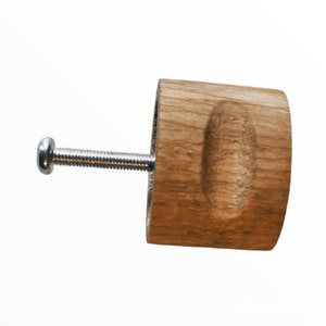 May include: A wooden knob with a rounded oval shape and a silver screw. The knob is light brown and has a natural wood grain.
