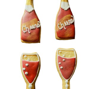 K&ouml;nnte beinhalten: Vier dekorierte Kekse in Form von Champagnerflaschen und -gl&auml;sern. Die Flaschen sind rot mit goldenen Akzenten und dem Wort "Cheers" in wei&szlig;em Zuckerguss. Die Gl&auml;ser sind mit roter Fl&uuml;ssigkeit gef&uuml;llt und haben wei&szlig;e Blasendetails.