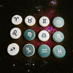 May include: A dozen round cookies decorated with zodiac symbols. Each cookie has a white or teal background with a different black or white astrological symbol. The cookies are arranged on a dark background with a starry design.