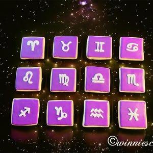 May include: Twelve square cookies decorated with purple frosting and white zodiac symbols. Each cookie represents a different astrological sign. The cookies are arranged on a dark background with a starry effect. The image includes the text "©winniescakes".