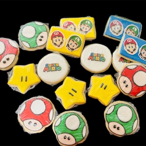 Könnte beinhalten: Eine Sammlung dekorierter Zuckerkekse mit Super Mario-Charakteren und -Designs. Die Kekse umfassen rote und weiße Pilze, grüne und weiße Pilze, gelbe Sterne und Kekse mit Mario und Luigi. Einige Kekse tragen die Aufschrift "Super Mario".