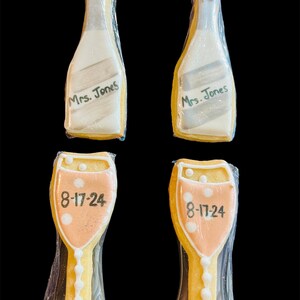 K&ouml;nnte beinhalten: Vier dekorierte Kekse. Zwei sind champagnerflaschenf&ouml;rmig, mit der Aufschrift "Mrs. Jones". Die anderen beiden sind champagnerglasf&ouml;rmig, mit dem Datum "8-17-24". Alle Kekse sind in durchsichtigem Zellophan verpackt.