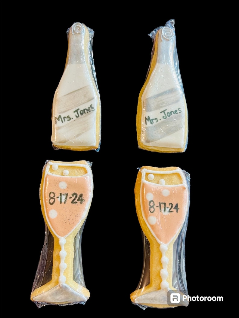 K&ouml;nnte beinhalten: Vier dekorierte Kekse. Zwei sind champagnerflaschenf&ouml;rmig, mit der Aufschrift "Mrs. Jones". Die anderen beiden sind champagnerglasf&ouml;rmig, mit dem Datum "8-17-24". Alle Kekse sind in durchsichtigem Zellophan verpackt.