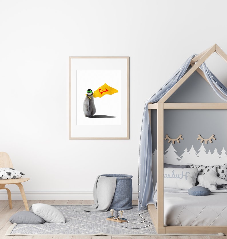 May include: A framed print of a penguin wearing a yellow cape with a red letter 'P' on it. The penguin is standing on a white background.