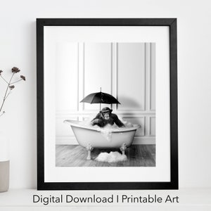 Peut inclure: Une photographie en noir et blanc d'un chimpanzé assis dans une baignoire avec des bulles. Le chimpanzé tient un parapluie au-dessus de sa tête. La baignoire est dans une salle de bain carrelée de blanc.