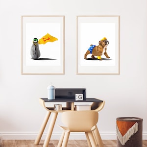 May include: Two framed illustrations of animals dressed as superheroes. The first image shows a penguin wearing a yellow cape with a red letter 'P' on it. The second image shows a bulldog wearing a blue and yellow Wonder Woman costume. The illustrations are displayed on a white wall above a wooden desk with a chair.