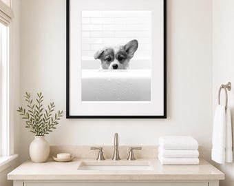 May include: A black and white framed wall art print featuring a Corgi dog peeking over the edge of a white bathtub. The dog has one ear standing up and one ear folded down. The background shows white subway tiles above the bathtub edge.