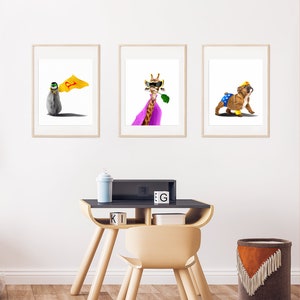 May include: Three framed animal illustrations in a children's room. The illustrations feature a penguin wearing a cape, a giraffe wearing a cape and sunglasses, and a bulldog wearing a cape and a crown. The illustrations are hanging on a white wall above a wooden desk and chair.