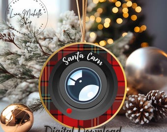 Könnte beinhalten: Ein runder Weihnachtsbaumschmuck mit einem rot-schwarzen Karomuster. Der Schmuck zeigt eine Kameraobjektiv mit dem Text "Santa Cam" in einem weißen Kreis.